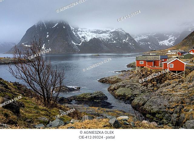 Fishing village at waterfront below snowy, craggy mountains, Hamnoya, Lofoten, Norway