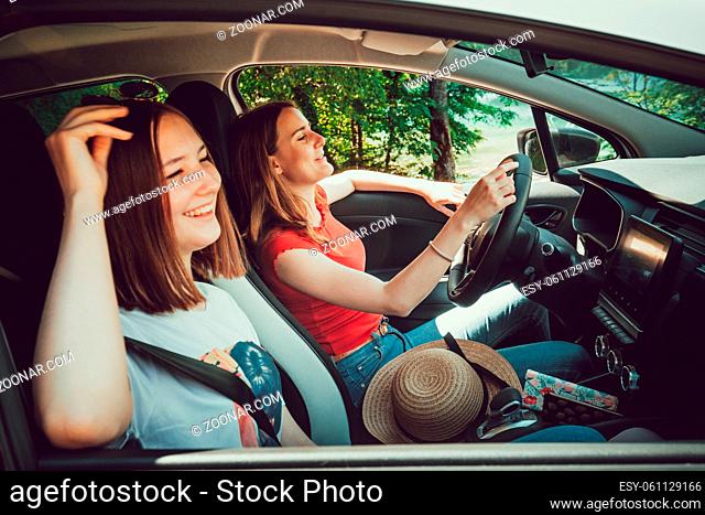 Two young girls listening to good music while driving in car, enjoy summer road trip in nature