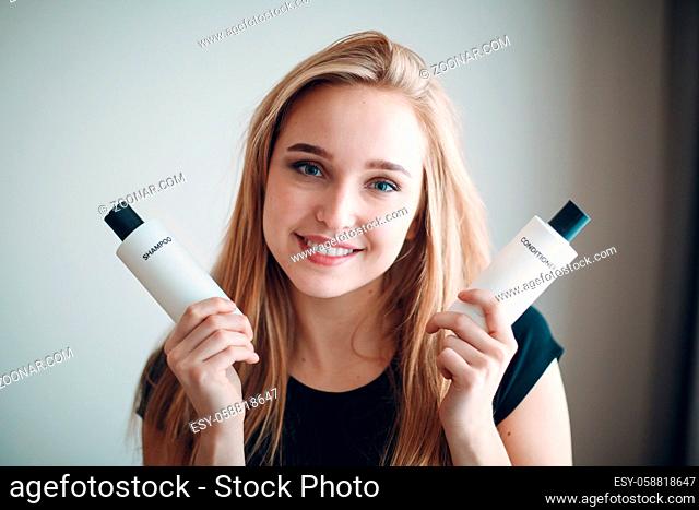 Pretty young woman hold two bottle with empty space. Shampoo and conditioner