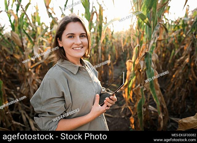 Portrait of smiling woman with digital tablet in maize field