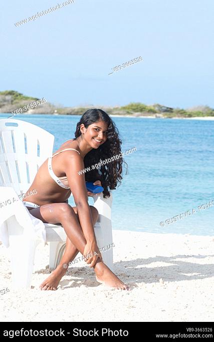 YOUNG African American WOMAN applying Sunscreen Lotion on legs at Caribbean Beach on the beach chair
