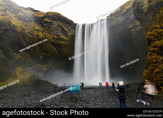 The Iconic Skogafoss Waterfall In Iceland. There are unrecognizable tourist people with motion blur in the foreground