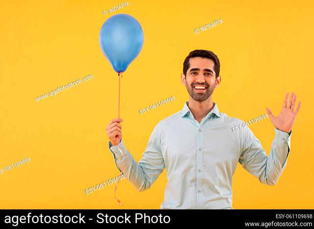 Portrait of happy young man holding balloon in hand and gesturing with palm