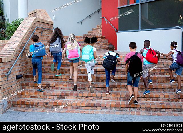 Rear view of group of diverse students with backpacks climbing up the stairs together at school