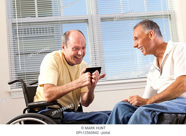 Two disabled men sitting in wheelchairs using a smart phone