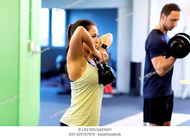 sport, fitness, lifestyle and people concept - woman with kettlebell and man with dumbbell exercising in gym