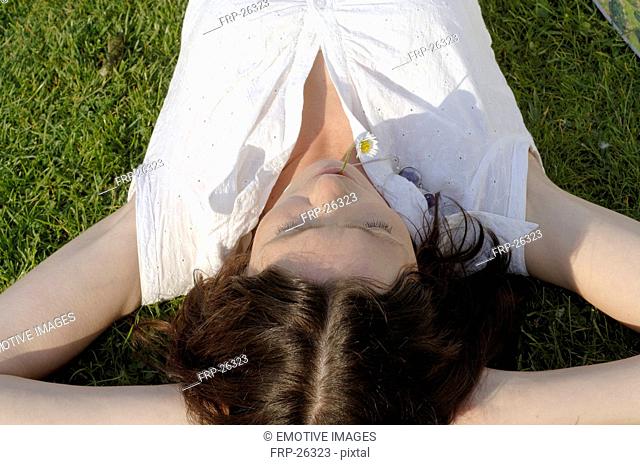 Woman lying in grass with daisy in her mouth