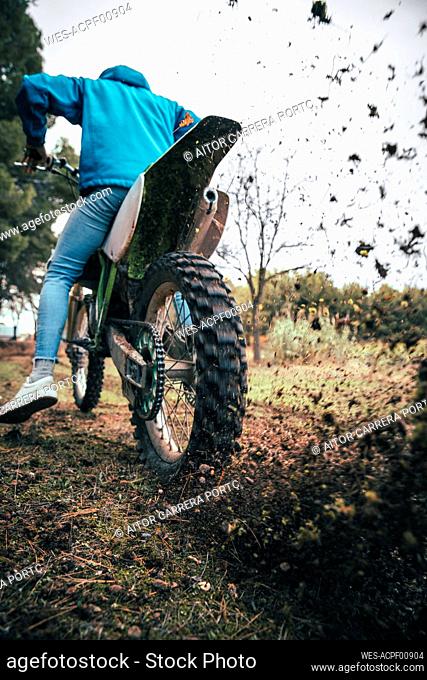 Male teenage rider spinning motorcycle tire while blowing dirt in forest during autumn