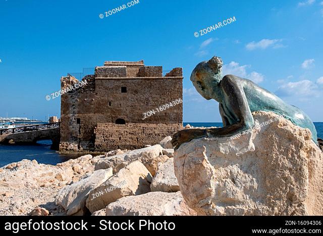 PAPHOS, CYPRUS - September 13, 2020: A bronze statue of woman called Sol Alter on a stone looking at the Paphos castle in the harbor