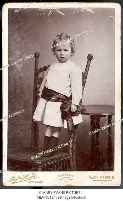 Photograph of a little boy, possibly Vincent Hope Davenport, standing on a chair in the photographer's studio: he wears a mourning sash round his waist