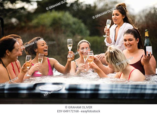 Small group of female friends socialising and relaxing in the hot tub on a weekend away. They are celebrating with a glass of champagne