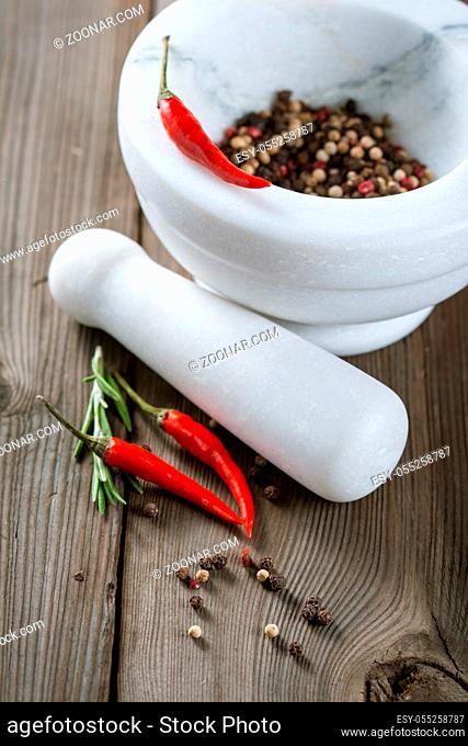 Mortar with different kinds of pepper and rosemary sprigs