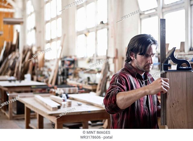 Caucasian man factory worker checking square measurements on a wooden part in a woodworking factory