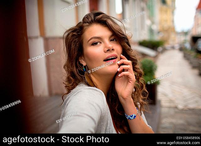 Selfie shot of young travel woman with nice street on the background. Beautiful girl with misterious look