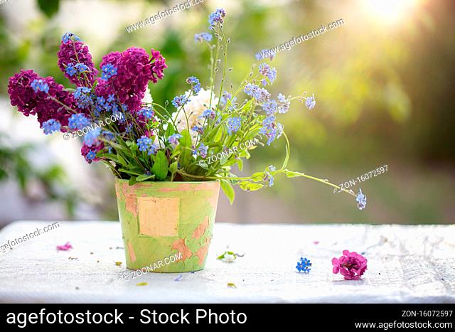 Spring or summer background. A bouquet of wildflowers in an old flowerpot lit by sunlight. Beautiful flowers on a green background