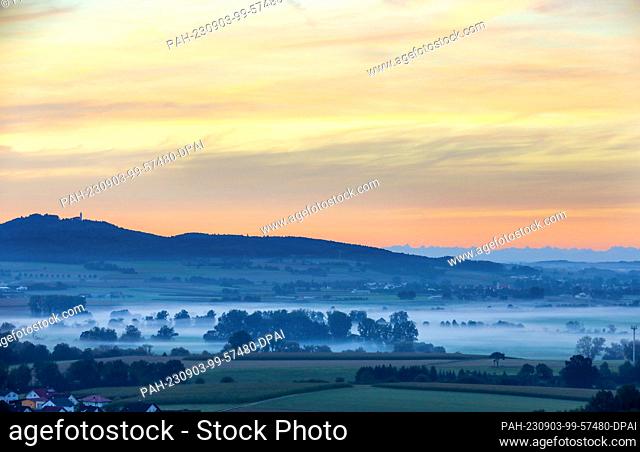 03 September 2023, Baden-Württemberg, Riedlingen: While morning fog has formed on the Danube, the sky above the pilgrimage church of St