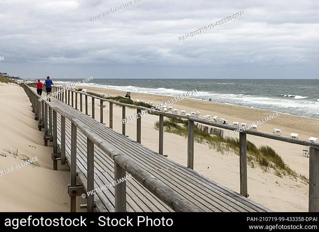 19 July 2021, Schleswig-Holstein, Westerland: A man and a woman are jogging on the beach of Westerland under a cloudy sky. Photo: Frank Molter/dpa