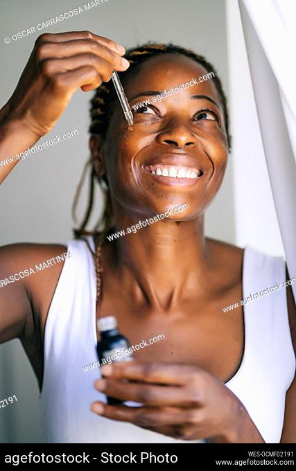 Smiling afro woman looking up while applying face serum