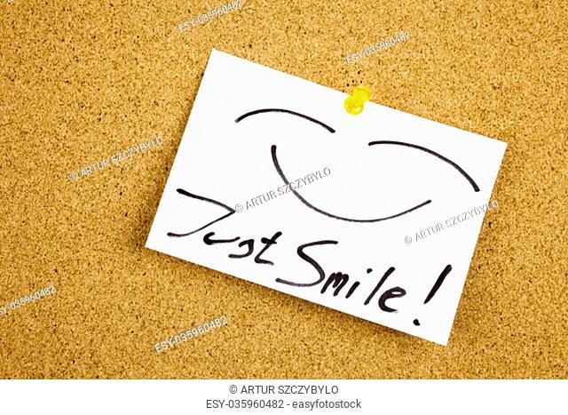 A yellow sticky note writing, caption, inscription Top view of Just Smile sticky note pasted in black ext on a sticky note pinned