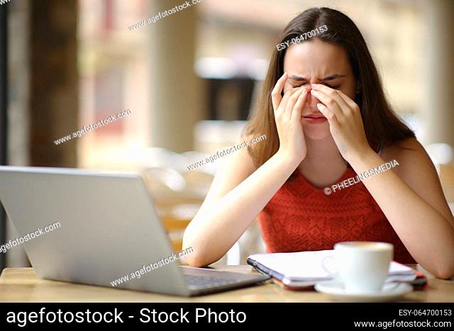 Front view portrait of a student suffering eyestrain after using laptop in a bar terrace