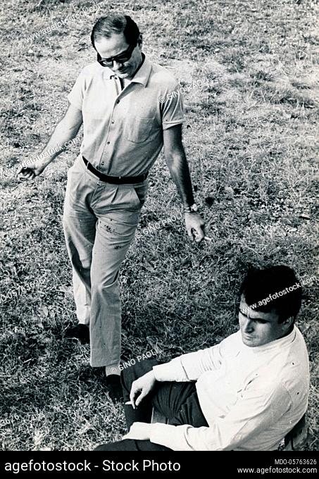 Italian singer-songwriter Gino Paoli smoking while standing on grassy field. 1960s