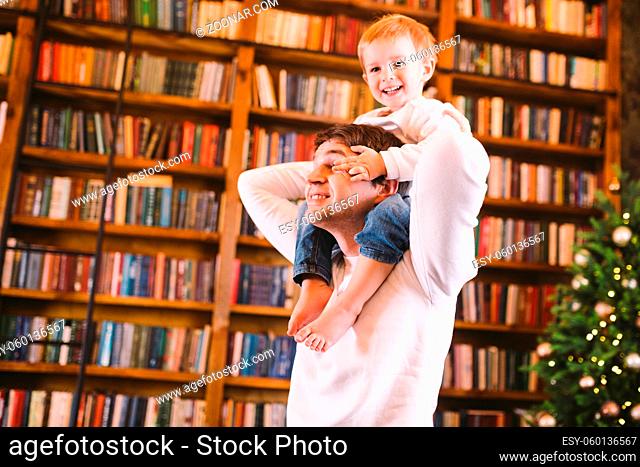 A cheerful and happy young father throws up, holds in his arms and around his neck his little son during a great active pastime at home near a Christmas tree...