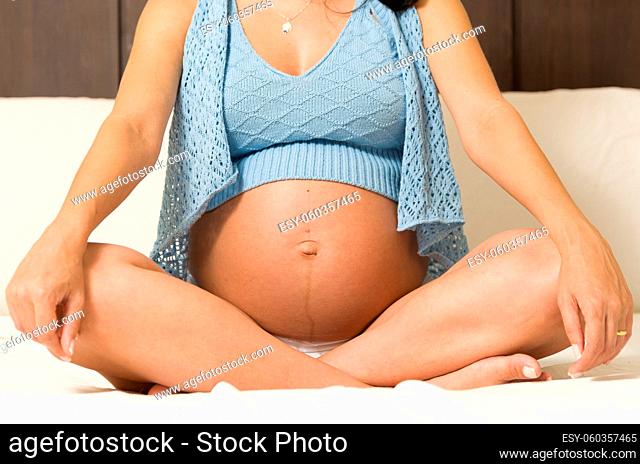 Pregnancy, rest, people and expectation concept - happy pregnant woman sitting on bed and touching her belly at home