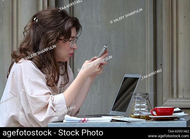 RUSSIA, MOSCOW - AGOSTO 8, 2023: Una mujer utiliza su teléfono inteligente en una cafetería acera en la calle Malaya Bronnaya. Valery Sharifulin/TASS