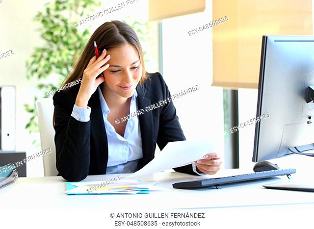 Businesswoman reading a document sitting in a desktop at office