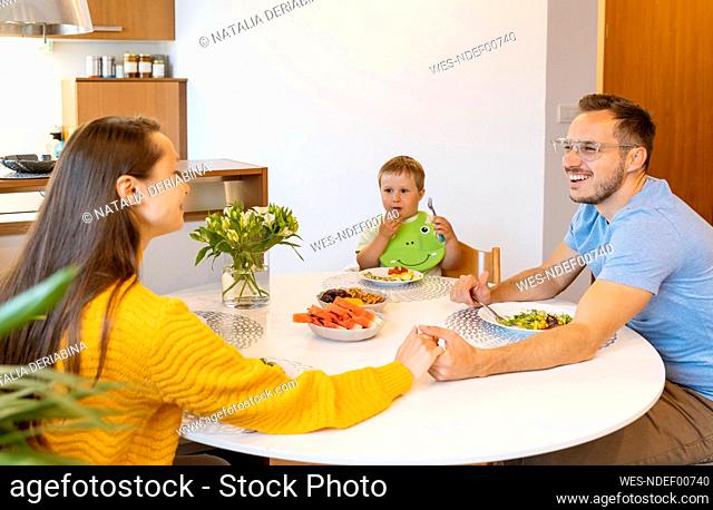Boy looking at smiling parents holding hands at dining table