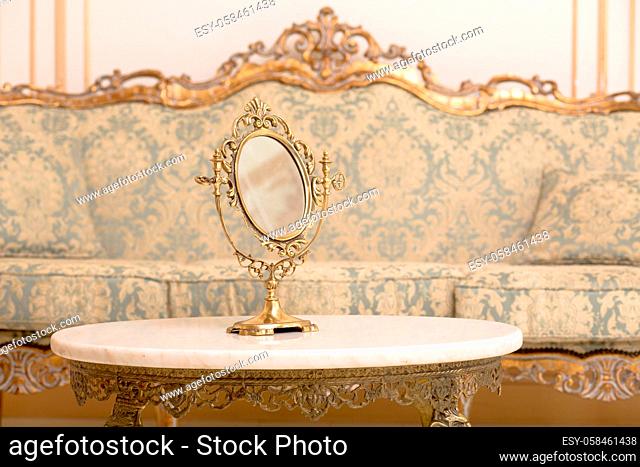 Royal golden frame on table in vintage interior. Closeup of mirror represented on table in royal apartment. Royalty concept