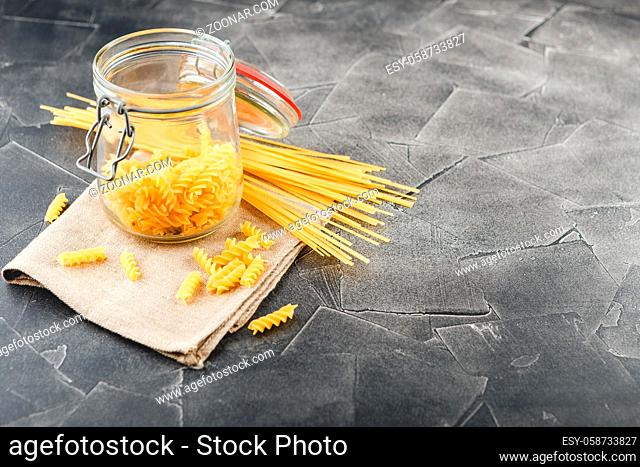 Different uncooked pasta in glass jar on table on dark background