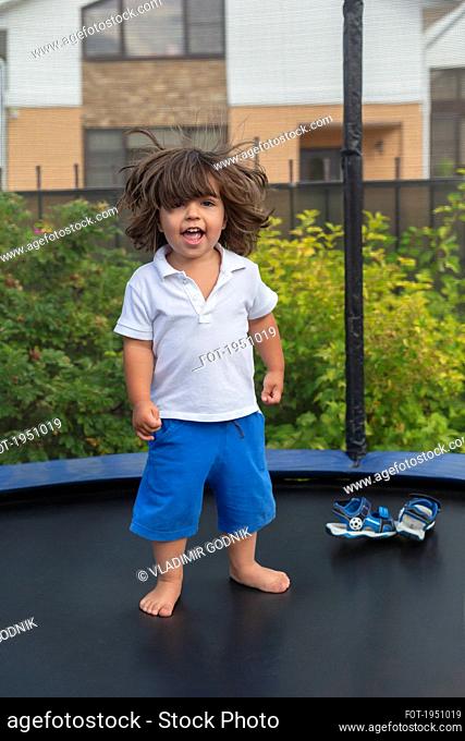 Portrait happy, cute toddler boy on backyard trampoline