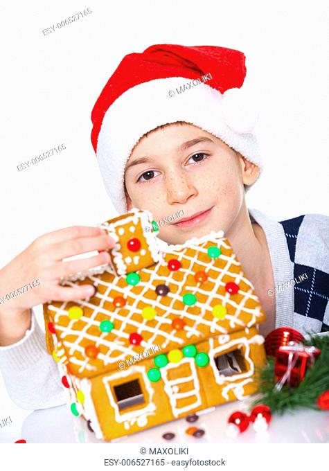 Christmas theme - Smiling boy in Santa's hat with gingerbread house, isolated on white