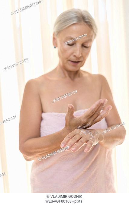 Senior woman applying cream on hands in the morning
