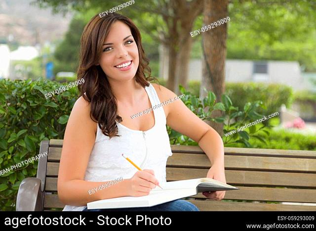 Attractive Young Adult Female Student on Bench Outdoors with Books and Pencil