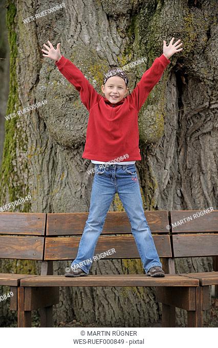 Germany, Bavaria, Girl standing on bench with arms up, portrait