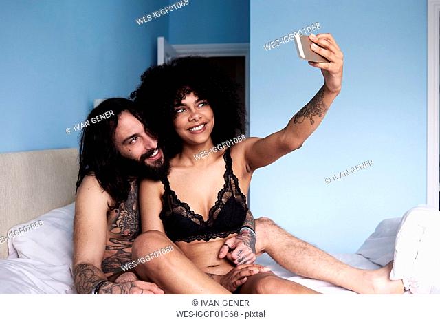 Happy affectionate young couple taking a selfie in bed