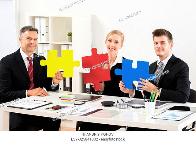 Team Of Happy Businesspeople Holding Multi-colored Jigsaw Puzzle In Office