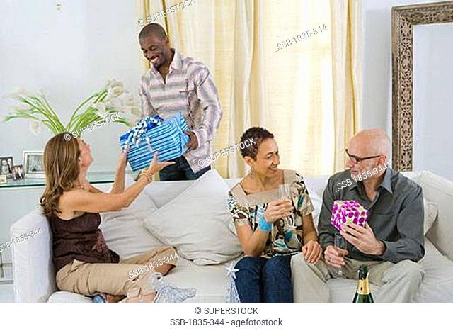 Man taking a gift from a woman sitting on a couch with her two friends