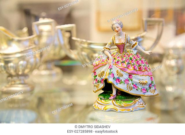Color vintage porcelain doll in the blurry background. The doll depicts a medieval lady in a ball gown. Porcelain doll in vintage interior