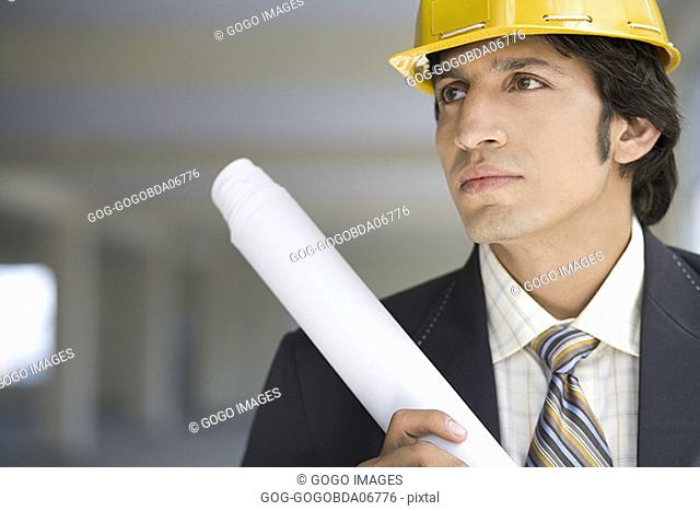 Businessman in hardhat carrying blueprints