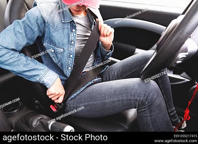 A hipster girl wearing jeans clothes fastens her seat belt in the car. Conception of safe driving