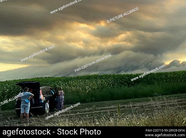 14 July 2022, France, La Teste-De-Buch: Tourists stand on the side of the road and look at the clouds of smoke from a forest fire on the Atlantic coast about 60...