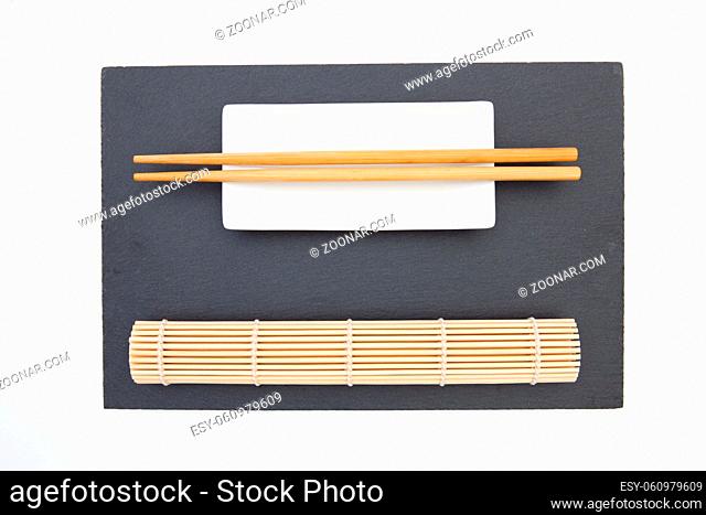 Rectangular slate plate with chopsticks, ceramic plate, bamboo mat for sushi on the white table