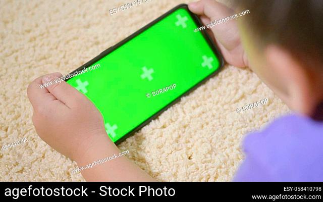 Asian kid boy preschool with gadget playing video games digital on mobile phone at home. Little child using and holding a smartphone green screen in hand
