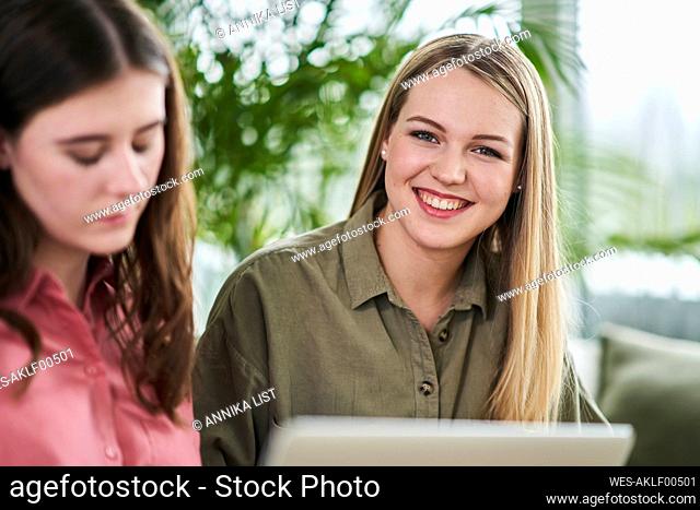 Happy blond female trainee sitting by businesswoman in office
