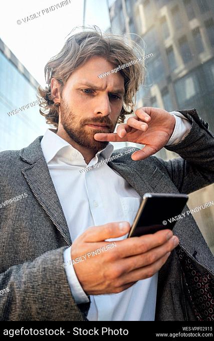 Worried young male entrepreneur using smart phone at financial district in city