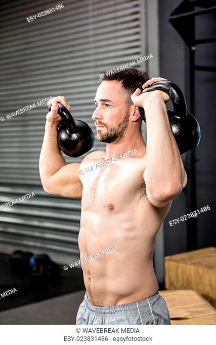 Shirtless man lifting kettlebells