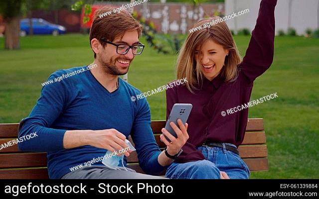 Happy news concept. Two friends find out end of covid-19 news Coronavirus pandemic is over. Take off their masks exclaimed joy Couple sitting on bench outdoor